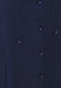 Vestito camicia blu navy con frontale a bottoni, caratterizzato da sei bottoni rotondi e due tasche sul petto, realizzato in un tessuto liscio con una leggera lucentezza.