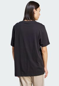 Camiseta de algodón negra con mangas cortas, corte relajado, cuello redondo y una parte trasera lisa. Presenta costuras mínimas y sin logotipos visibles.