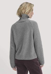 Grauer Strickpullover mit hohem Kragen, gerippten Bündchen und Saum; bietet einen lässigen Schnitt und Raglanärmel. Der Stoff wirkt weich und strukturiert.