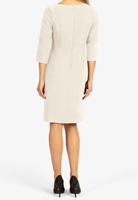 Robe gris clair avec manches trois-quarts, taille cintrée et ourlet à hauteur des genoux. Comprend une fermeture éclair au dos et un design structuré.