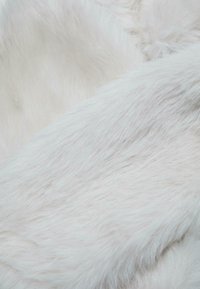 Primo piano di una morbida trama in pelliccia sintetica bianca con lunghe fibre setose che creano una superficie liscia e soffice.