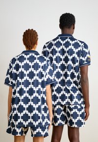 Kortärmade toppar och shorts i marinblått med ett vitt geometriskt mönster. Avslappnad passform och smidigt tyg med kontrasterande detaljer.