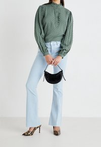 Zielona bluzka o teksturze z falbaniastym kołnierzykiem, w zestawie z jasnoniebieskimi spodniami dzwonami i czółenkami w panterkę. Czarna torebka o zaokrąglonym kształcie.