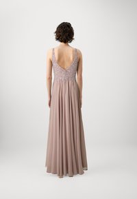 Duga, lepršava haljina od mekanog blush materijala s dubokim izrezom na leđima. Bodice se ističe složenim perlama, što dodatno naglašava ukupni elegantan dizajn.