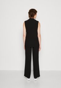 Black sleeveless top with a collar, paired with black wide-leg trousers. The outfit has a smooth texture and features a clean, tailored design.