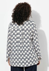 Camicia a manica lunga con un motivo geometrico in blu navy e crema. Presenta una vestibilità ampia, un orlo arrotondato e delle fessure laterali per facilitare i movimenti.