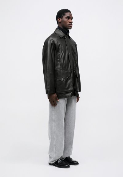 Melnas ādas jaka ar apkakli, priekšējiem kabatām un pogu aizdari, kombinēta ar pelēkām platām biksēm un melniem loafers.