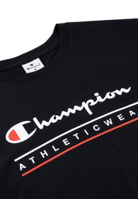 Camiseta de algodón negra con cuello redondo y mangas cortas. Presenta un gran logotipo blanco de "Champion" y detalles rojos, etiquetada como "ATHLETICWEAR".