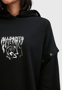 Sweat à capuche noir avec texte blanc déformé "ALLSAINTS" sur la poitrine et boutons-pression le long de la manche supérieure.