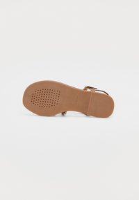 Brun sandal med en texturerad sula, med platt design, vristrem och perforerade detaljer för andningsförmåga.