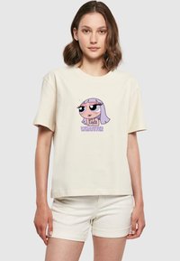 Jeune femme portant un T-shirt crème avec une fille de bande dessinée aux cheveux violets et le mot "WHATEVER" en texte violet.