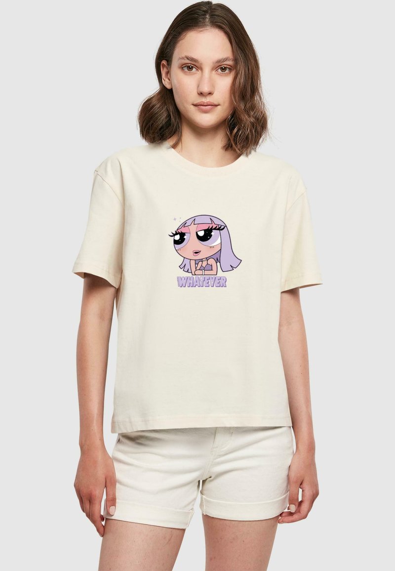Jeune femme portant un T-shirt crème avec une fille de bande dessinée aux cheveux violets et le mot "WHATEVER" en texte violet.