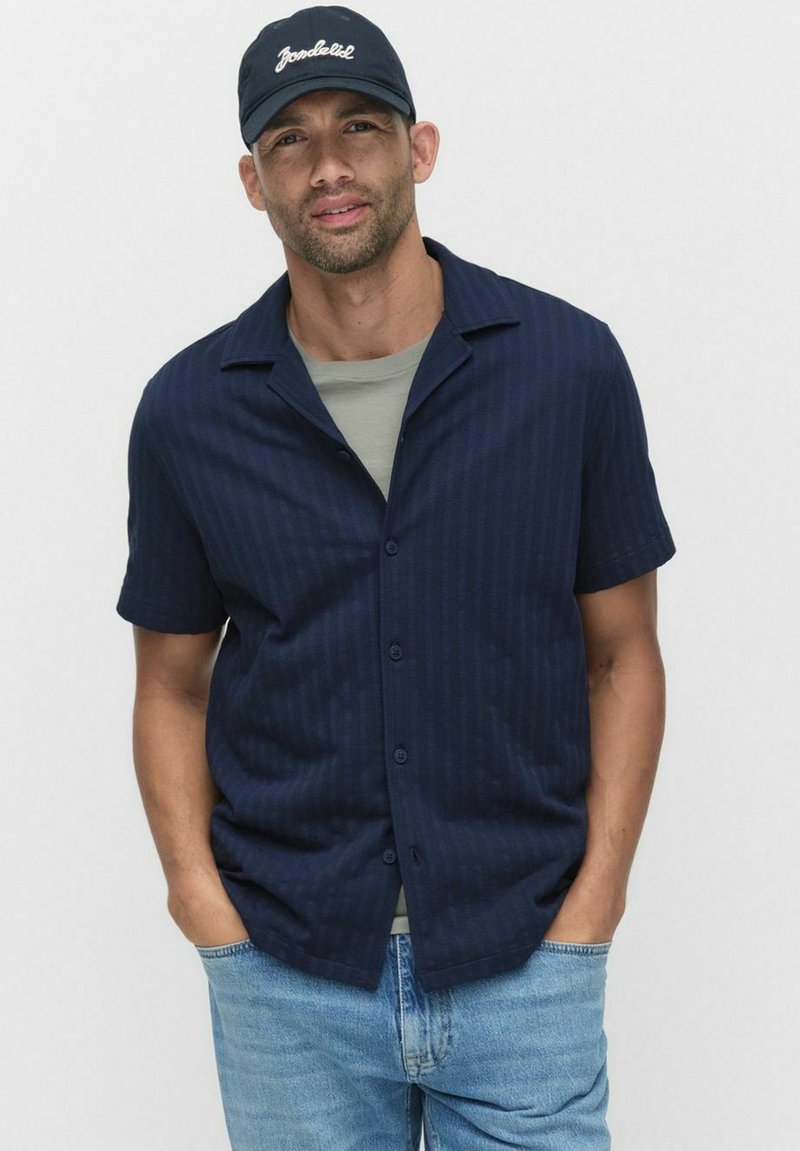 Korte mouwen, marineblauwe overhemden met subtiele verticale strepen, gemaakt van lichte stof, gecombineerd met een grijs T-shirt eronder en blauwe jeans.