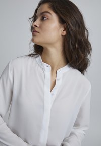 White button-up shirt made of lightweight, sheer fabric. Features a mandarin collar, front placket with buttons, and long sleeves.
