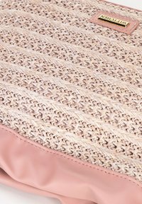 Materiale tessuto beige con texture, con accenti in finta pelle rosa. Presenta un'etichetta con logo dorato. Forma rettangolare con una base morbida e flessibile.