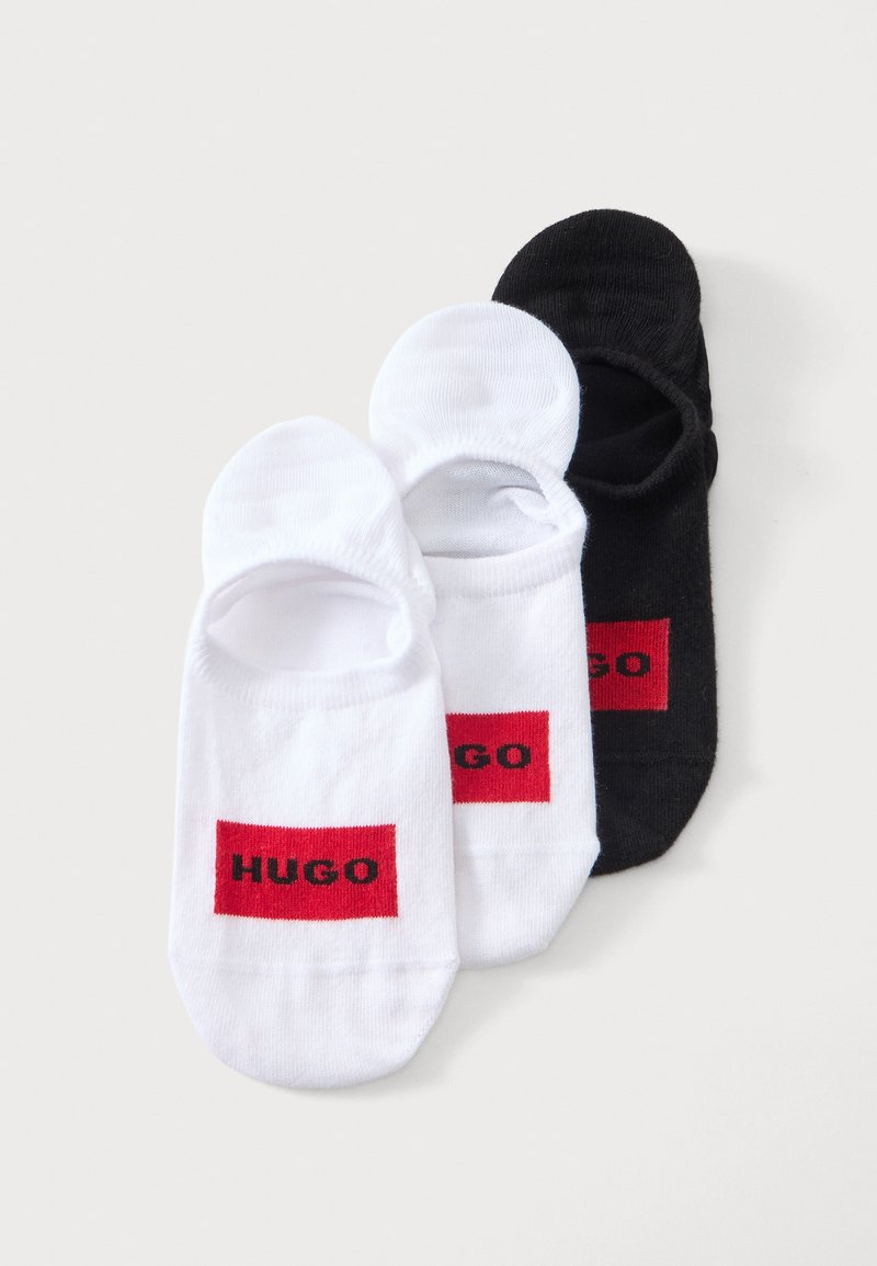 Deux paires de chaussettes invisibles blanches et une paire de chaussettes invisibles noires avec des patchs rectangulaires rouges portant la mention HUGO.