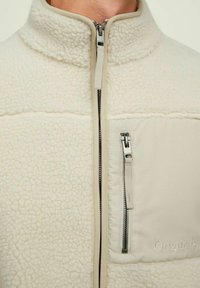 Giacca in pile color crema con zip frontale e tasca sul petto con zip etichettata "Originals."