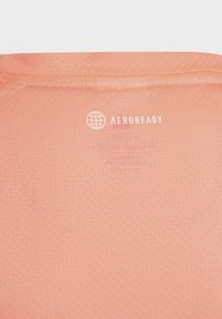 Camiseta Aeroready de color rosa claro que presenta una tela suave y texturizada con un sutil patrón y una marca blanca impresa cerca del cuello.