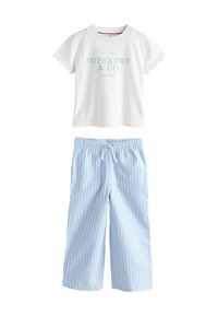 Balta īsām piedurknēm T-kreklā ar uzrakstu "Superdry & Co New York", apvienota ar gaiši ziliem plašajiem biksēm ar baltām vertikālām svītrām un stiept auklu jostasvietā.