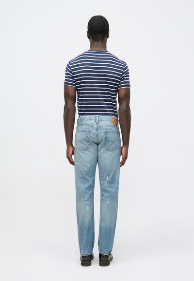 Plave traperice s laganim izblijedjelim učinkom i ravnim krojem, uparene s mornarsko plavom i bijelom prugastom majicom. Vidljive su istaknute šavove i detalji zakrpa.