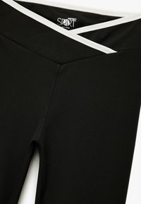 Zwarte sportlegging met een brede tailleband met een witte accent. Gemaakt van rekbare stof met een soepele textuur en verstevigde naden.