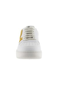 Zapatilla blanca con puntera perforada, cordones beige y un logo "V" texturizado en amarillo en el lateral, vista frontal.