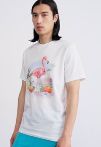 Hvid bomulds T-shirt med et farverigt flamingo- og tropisk design, med lyserøde og orange accenter. Korte ærmer og rund hals stil.