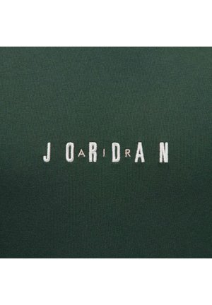 Zielony materiał z haftowanym napisem "JORDAN" w kolorze białym i jasnoróżowym. Tekstura jest gładka, z lekkim naciągiem. Projekt charakteryzuje się wielkimi literami.