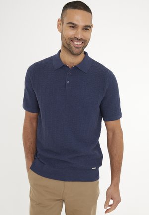 Marineblaues Kurzarm-Polohemd mit strukturiertem Strickmuster, Drei-Knopf-Leiste und geripptem Saum. Kombiniert mit khakifarbenen Hosen.