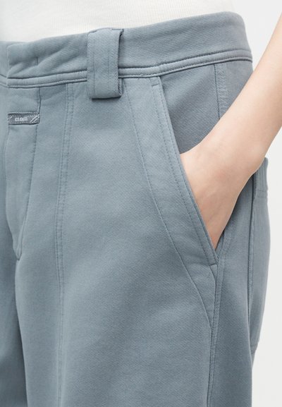 Χέρι στην πλευρική τσέπη ανοιχτό μπλε παντελονιού με ραμμένη εφαρμογή, θηλιά για ζώνη και μικρή ετικέτα ύφασμα με το λογότυπο κοντά στη μέση.