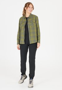 Grön och gul rutig skjorta med två bröstfickor, i kombination med svarta byxor och grå vandringsskor. Slät textur, avslappnad design.