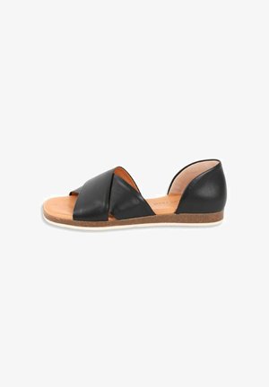 Black leather flat sandal with open toe, crisscross straps, cushioned tan footbed, and white-rimmed cork sole.