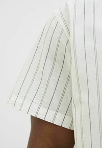 Cream short-sleeve shirt featuring vertical navy stripes, a relaxed fit, and a textured fabric, showcasing neat stitching along the hem.