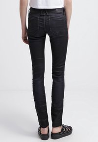 Svarta skinny jeans i denim med en mjuk textur, två bakfickor och en midja med medelhöjd. Matchas med svarta sandaler.