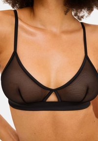 Zwarte mesh bralette met een driehoekige vorm, verstelbare bandjes en een sleutelgatdetail in het midden. Glad band onder de buste.