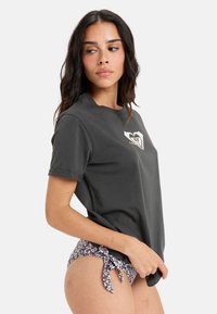 Grå bomulds T-shirt med korte opsmøgede ærmer, der har et frontgrafiklogo. Parret med badetights i blomstermønster med sidesnore.