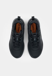 Black athletic shoes featuring a smooth, textured upper, contrasting brown insole, and lightweight sole with pull tabs for easy wear.