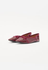 Ballerines en cuir vernis rouge avec un bout pointu, un détail en nœud à l'avant et un talon arrondi. Texture lisse et design minimaliste.