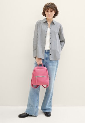 Sac à dos en cuir rose avec une finition texturée, poche avant zippée et deux bretelles, associé à une chemise à rayures et un jean ample.