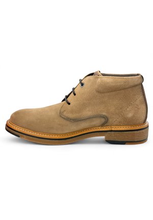 Bottines en daim marron à bout rond, avec deux œillets en métal noir et une semelle en caoutchouc brun clair avec un fil de couleur contrastante.