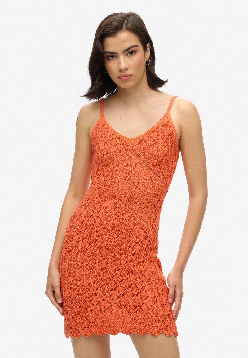 Gehaakt oranje jurk met een gegolfd patroon, spaghettibandjes en een aansluitende pasvorm. Textuurmateriaal creëert een open geweven ontwerp.