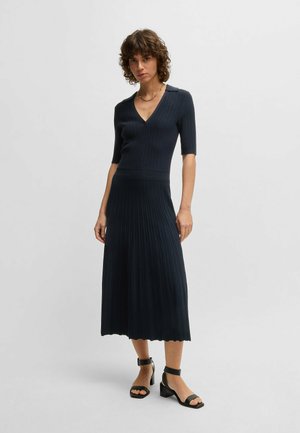 Dark ribbed dress with a V-neck, short sleeves, and pleated skirt. Features a fitted bodice, flowing skirt, and scalloped hemline.