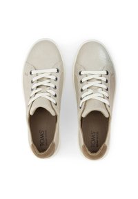 Un paio di sneakers beige TOMS con lacci bianchi e suola bianca, viste dall'alto su uno sfondo bianco.