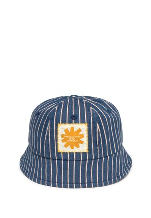 Modrý a biely klobúk s vertikálnymi pruhmi a štvorcovou žltou nášivkou na prednej strane s nápisom „Prírodné farbivá z Auroville“.