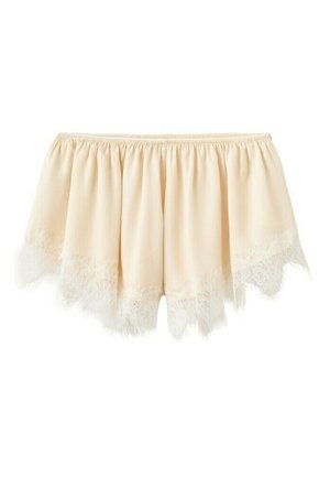 Blusa color crema con escote fuera del hombro con cuello elástico y delicado ribete de encaje a lo largo del dobladillo con bordes ondulados.