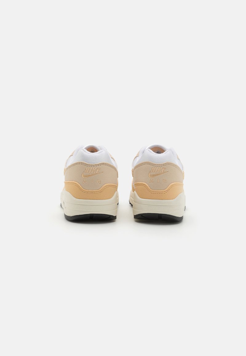 Zapatillas Nike Air con parte superior blanca y acentos en beige y durazno, tacón redondeado, material texturizado y suela negra.