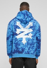 Haut à capuche tie-dye bleu avec un grand motif blanc au dos, en tissu doux avec une coupe décontractée, des poignets et un ourlet côtelés.