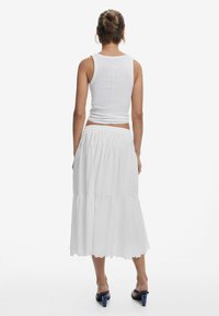 White, sleeveless tank top paired with a long, tiered white skirt. The skirt features a smocked waistband and scalloped hem. Blue heeled sandals.
