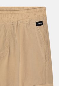 Beige bukser med elastisk talje, sidelommer og et lille sort "ASPESI" mærke tæt på den højre lomme.