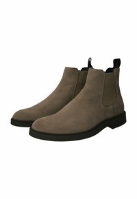Un par de botas Chelsea de ante topo con suelas negras y paneles laterales elásticos sobre un fondo blanco.